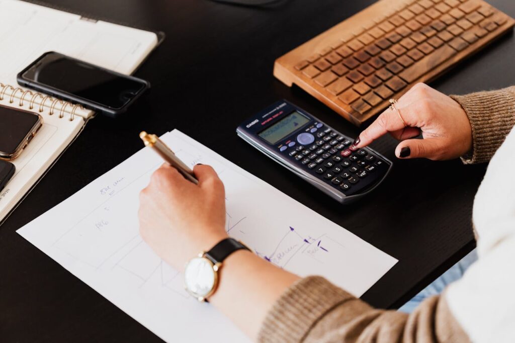 pexels photo 4476375 Close-up of hands working with a calculator and notebook on a desk, analyzing documents.